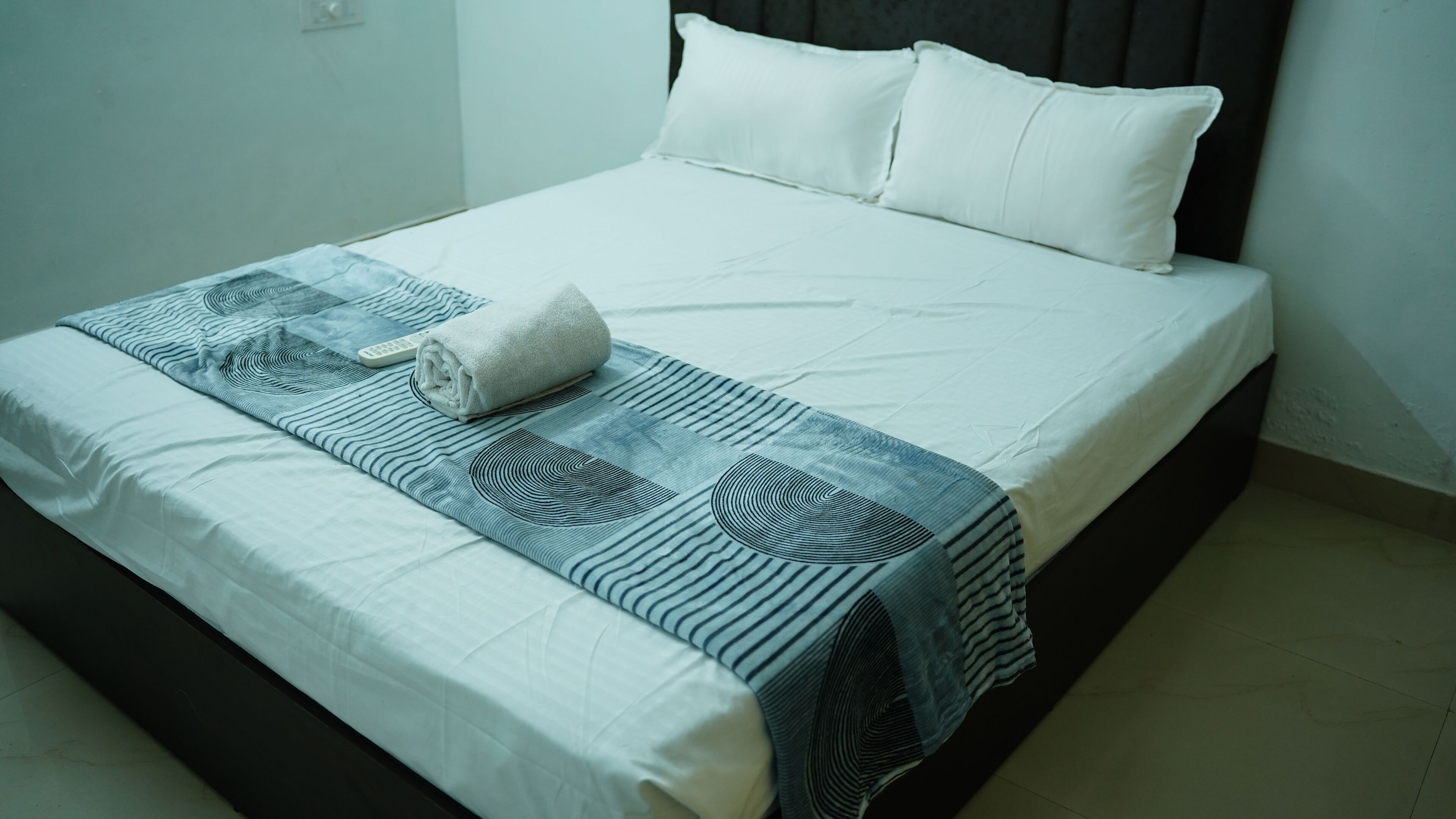 A neatly made bed with a white duvet, a rolled towel, and a patterned blanket.