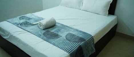 A neatly made bed with a white duvet, a rolled towel, and a patterned blanket.