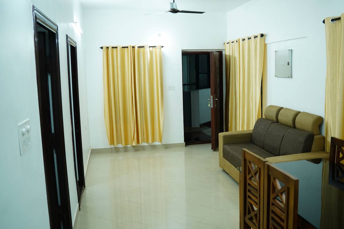 A living room with a sofa, a wooden chair, yellow curtains, and a ceiling fan.