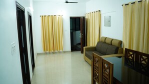 A living room with a sofa, a wooden chair, a ceiling fan, and yellow curtains. - Stay Ease Rental Rooms (Palakkad)