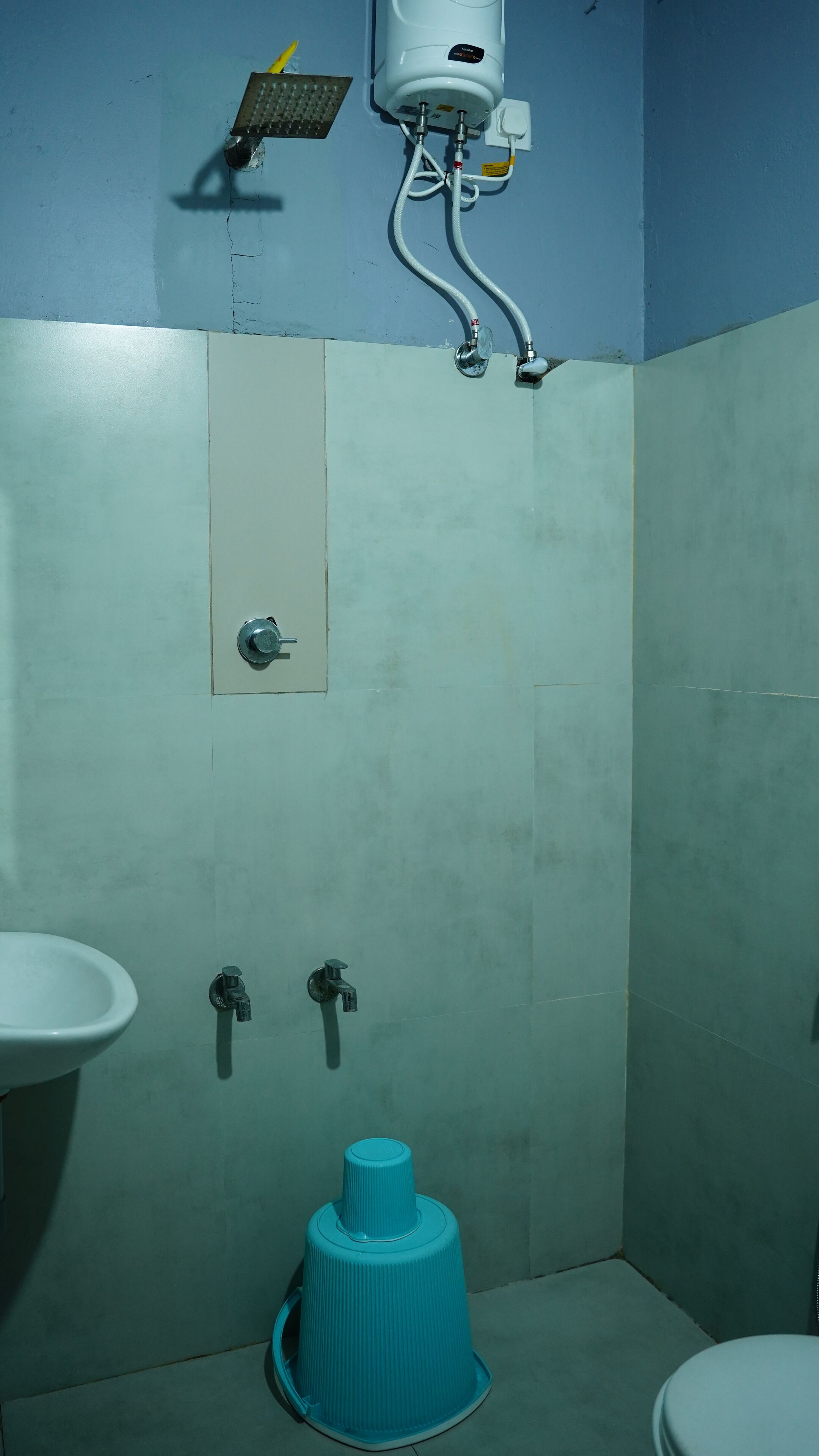 A bathroom with a sink, two faucets, a toilet, a trash bin, and a showerhead.