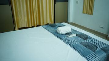 A neatly made bed with a white sheet, a rolled white towel, and a remote control on a blue and white patterned blanket.