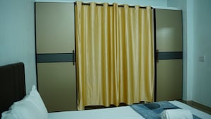 A room with a bed, a wardrobe with a curtain, and a wall socket. - Stay Ease Rental Rooms (Palakkad)