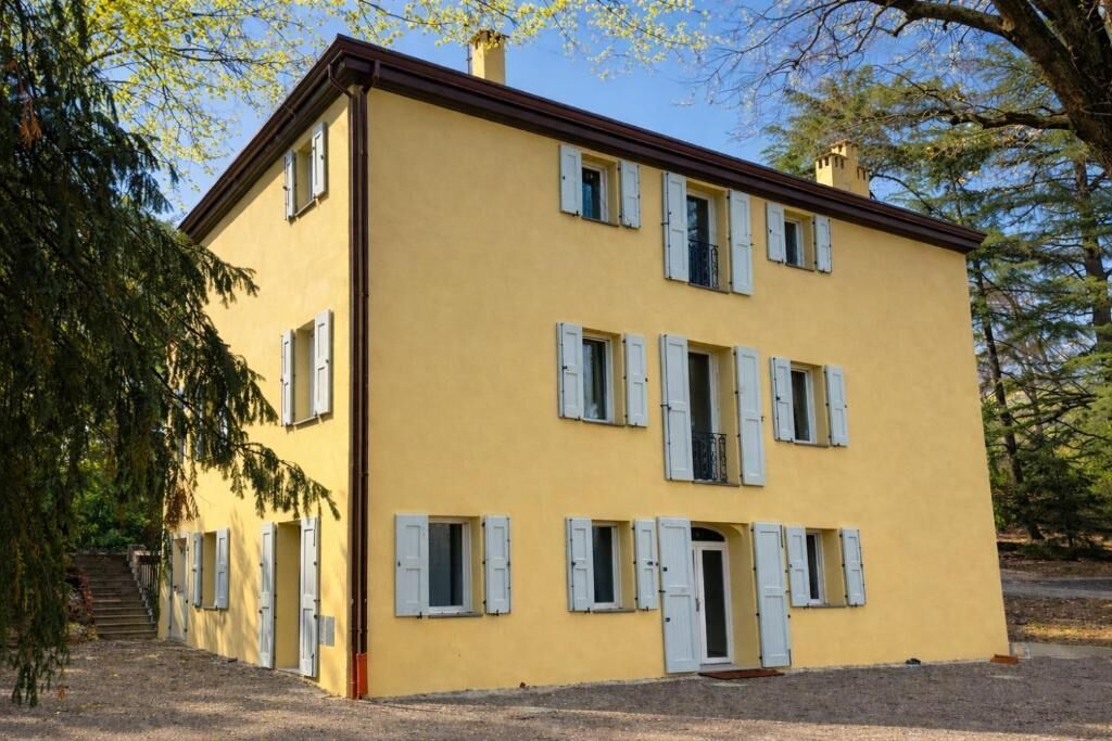 Un bâtiment jaune à deux étages, doté de volets blancs, d’une entrée centrale et d’un escalier menant à l’étage supérieur.