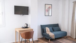 Ein modernes Wohnzimmer mit einem Holztisch, einem blauen Sofa, einem Wand-Fernseher und einem gerahmten Bild an der Wand.