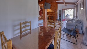 Ein Holzesstisch mit Stühlen, ein an der Wand montierter Fernseher und eine Couch im Hintergrund.