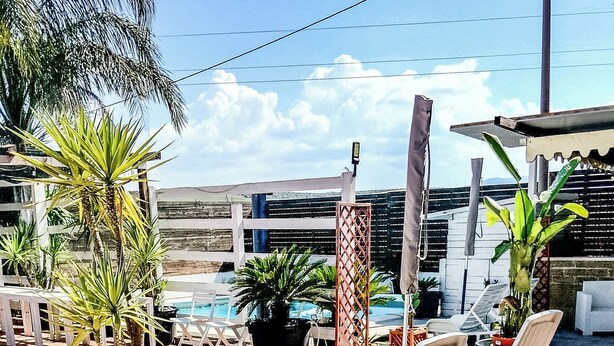 A poolside area with lounge chairs, potted plants, and a view of a building in the background. - Villa Lucia (Lucera)