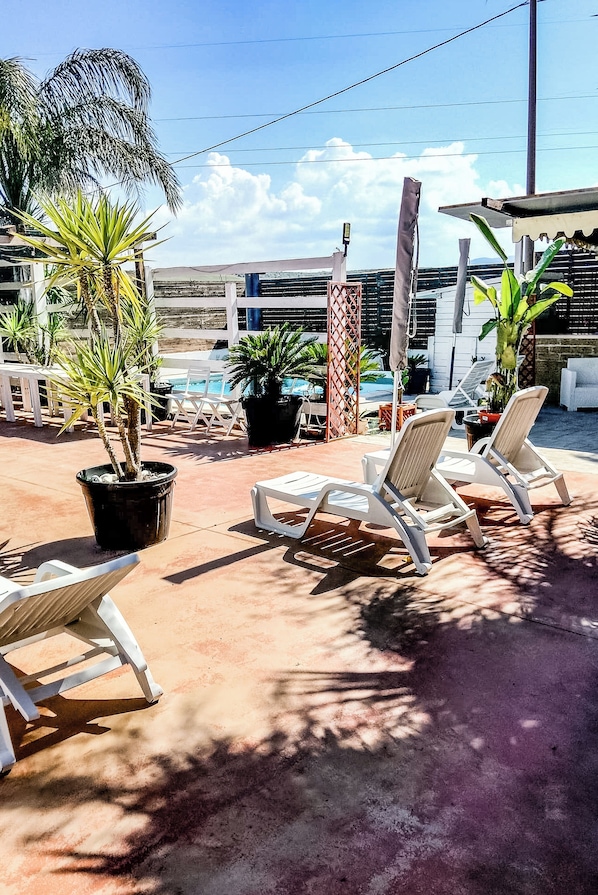 Un espace aménagé au bord de la piscine, avec des chaises longues, des plantes en pot et une vue sur un bùtiment en arriÚre-plan.