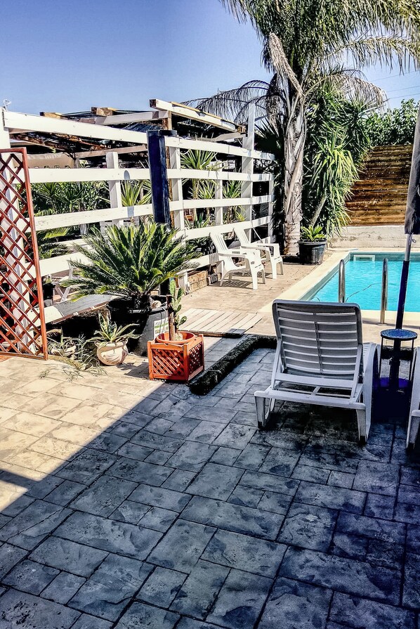 Un área de piscina con una valla blanca, sillones de descanso y plantas en macetas.