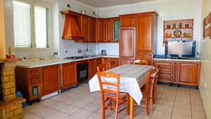 A kitchen with wooden cabinets, a dining table with chairs, a stove, and a refrigerator. - Villa Lucia (Lucera)