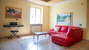 A living room with a red sofa, a small table, a keyboard, and two paintings on the walls. - Villa Lucia (Lucera)