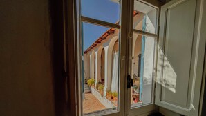 A room with a large window overlooking a courtyard with arches and potted plants. - Borgo Ferraria (Sinnai)