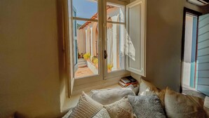 A room with a large window, a bed with pillows, and a nightstand with books. - Borgo Ferraria (Sinnai)