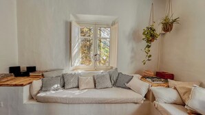 A cozy room with a white sofa, a small table with books and a plant, and a window with a view of trees. - Borgo Ferraria (Sinnai)