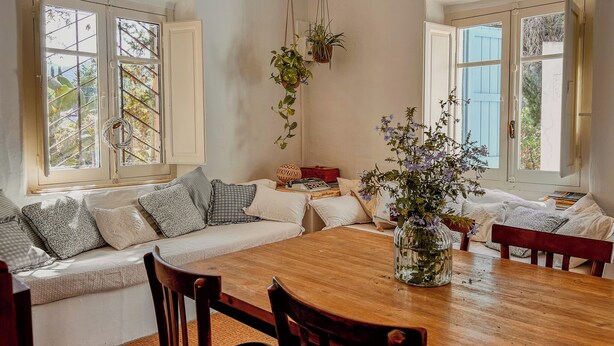 A cozy living room with a wooden dining table, two sofas with patterned cushions, and a hanging plant. - Borgo Ferraria (Sinnai)