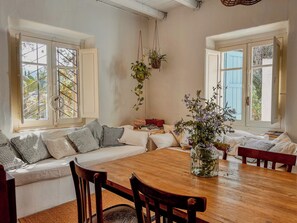 Un salon chaleureux avec une table à manger en bois, deux canapés ornés de coussins à motifs et une plante suspendue.