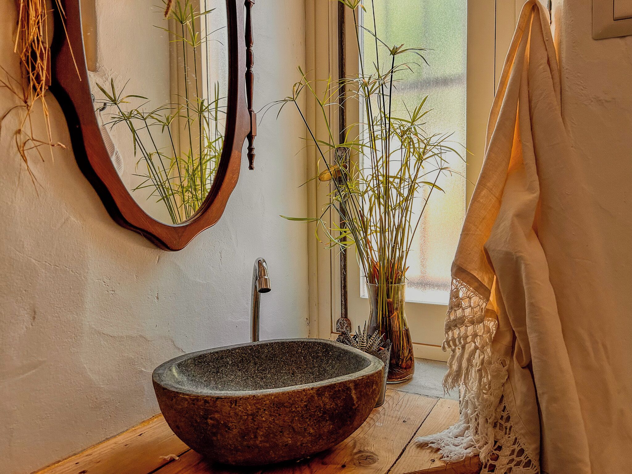 A bathroom with a stone sink, a wooden floor, a mirror, and bamboo plants.