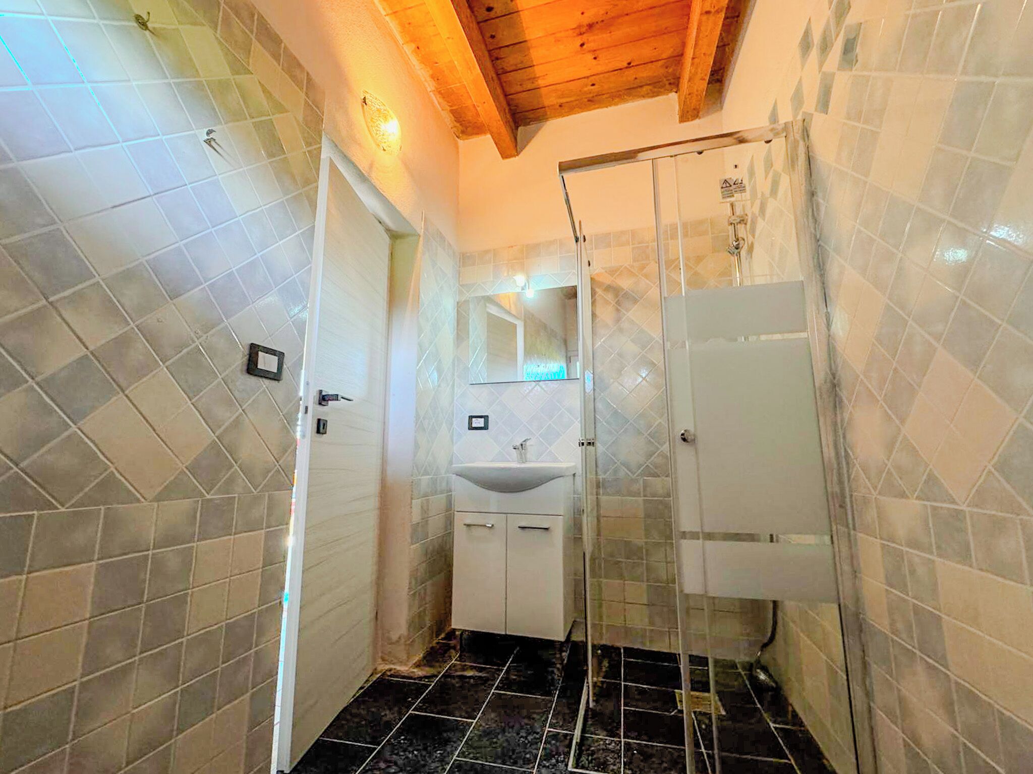 A bathroom with a tiled floor, a sink, and a shower area.