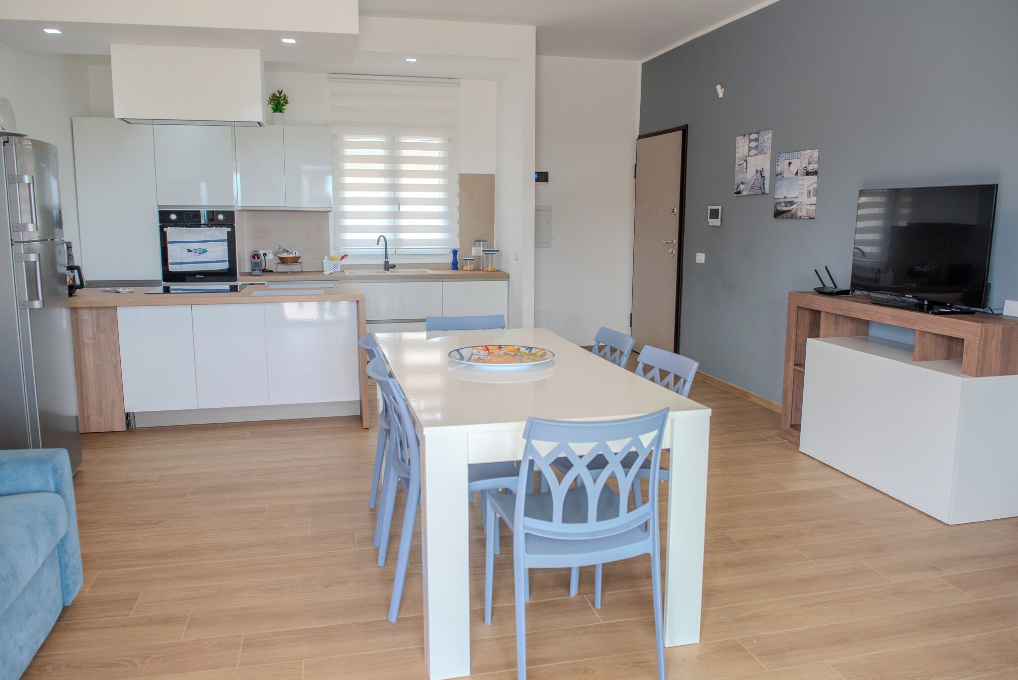 A modern kitchen with a built-in oven, a dining table with chairs, and a TV on a wooden stand.