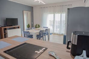 A modern kitchen with a dining area, a TV, and a refrigerator. - Villa Rosy (Butera)