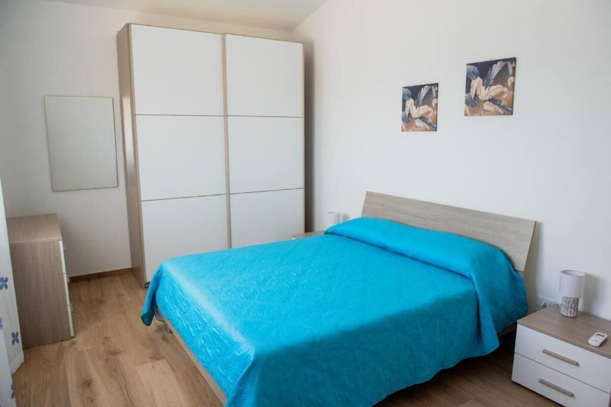 A bedroom with a bed, a wardrobe, a bedside table, and two wall-mounted paintings.
