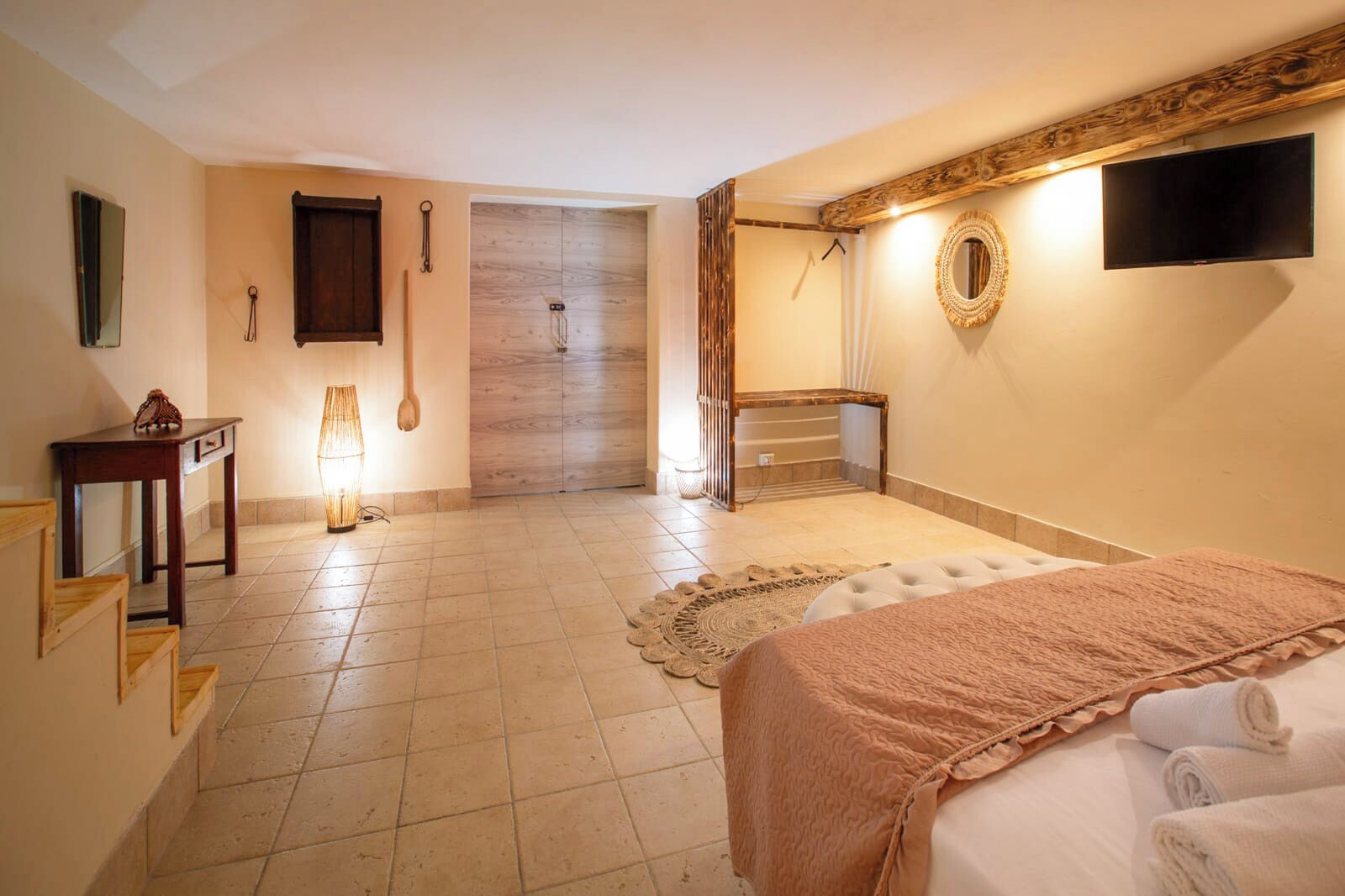 Habitació d'hotel amb llit, televisió penjada a la paret, porta de fusta, taula petita i làmpada.