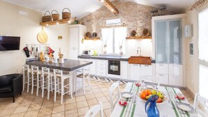 A modern kitchen with a stone wall, wooden beams, and a dining area with a table set for four. - Villetta Tra Mari E Monti (San Giovanni Rotondo)