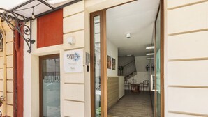 L’entrée d’un hôtel, avec une porte en verre, une enseigne et une vue sur un espace de restauration comprenant des chaises et une table.