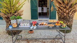 A table set up outside a building with green shutters, displaying various food items and a basket of eggs.