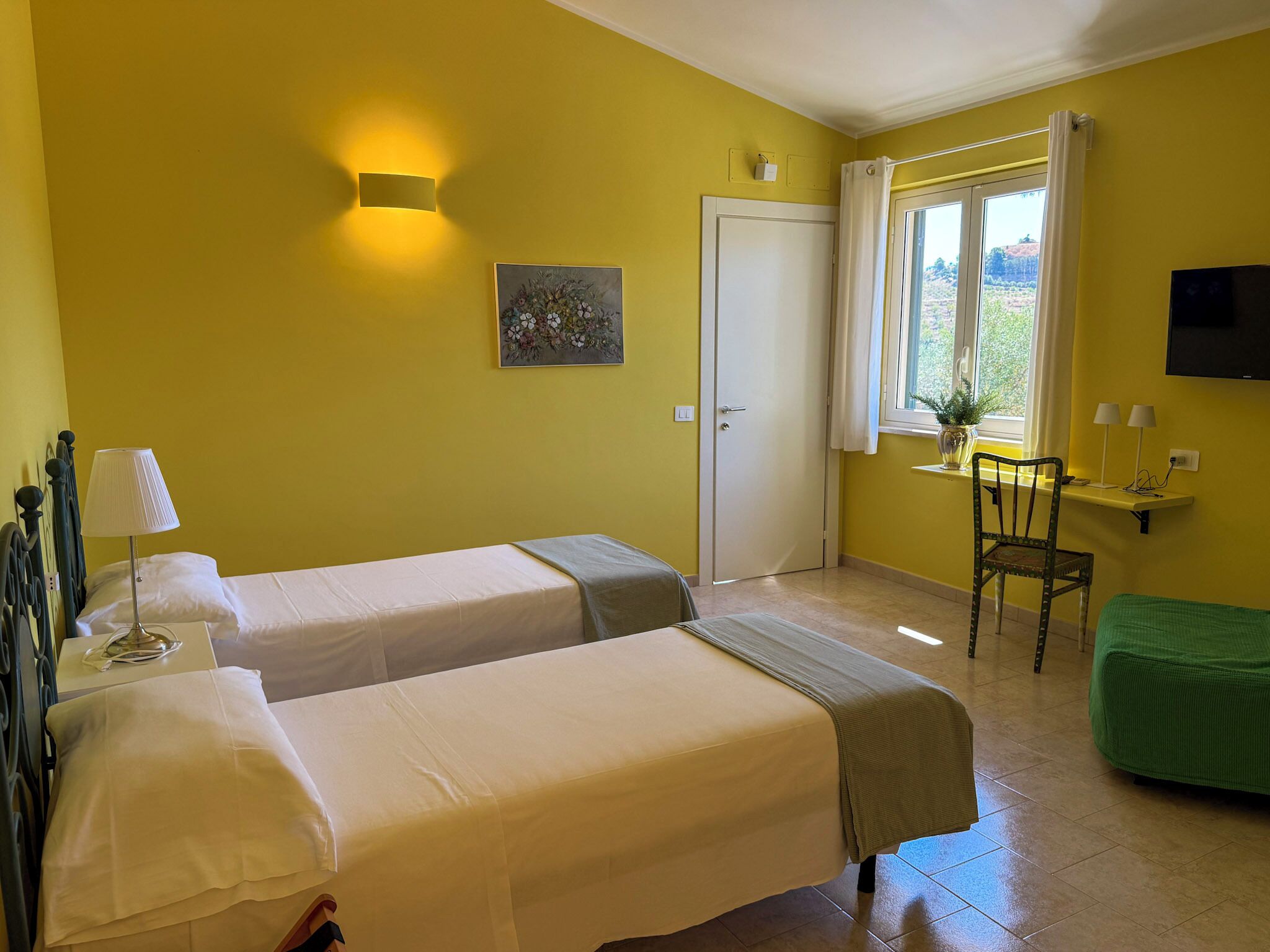 Ein Zimmer mit zwei Betten, einem Schreibtisch, einem Stuhl, einem Fernseher und einem Fenster mit Vorhängen.