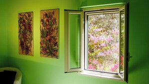 A room with a green wall, a window with a view of pink flowers, and two abstract paintings.