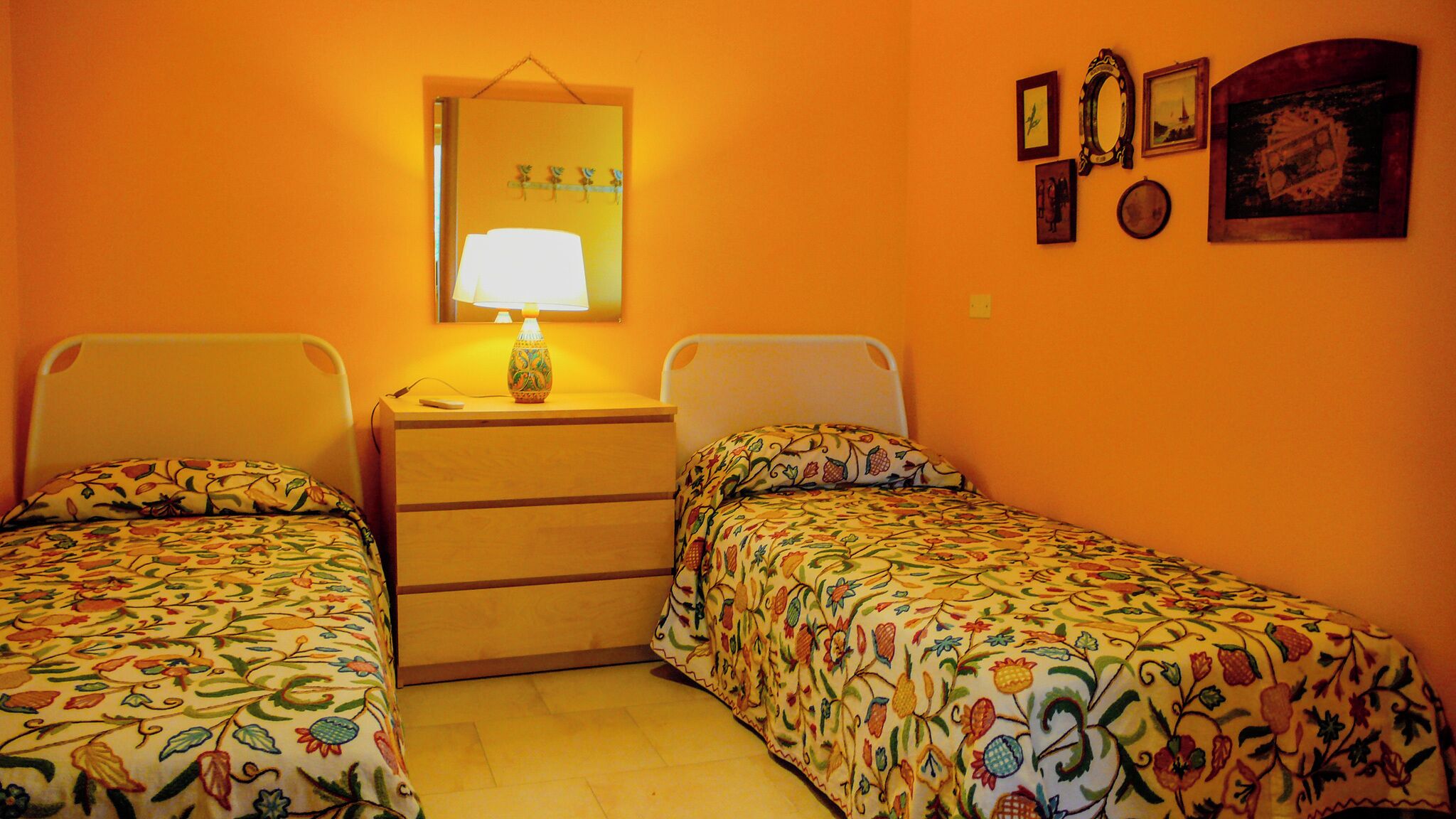 A room with two single beds, a dresser, a mirror, and a lamp.