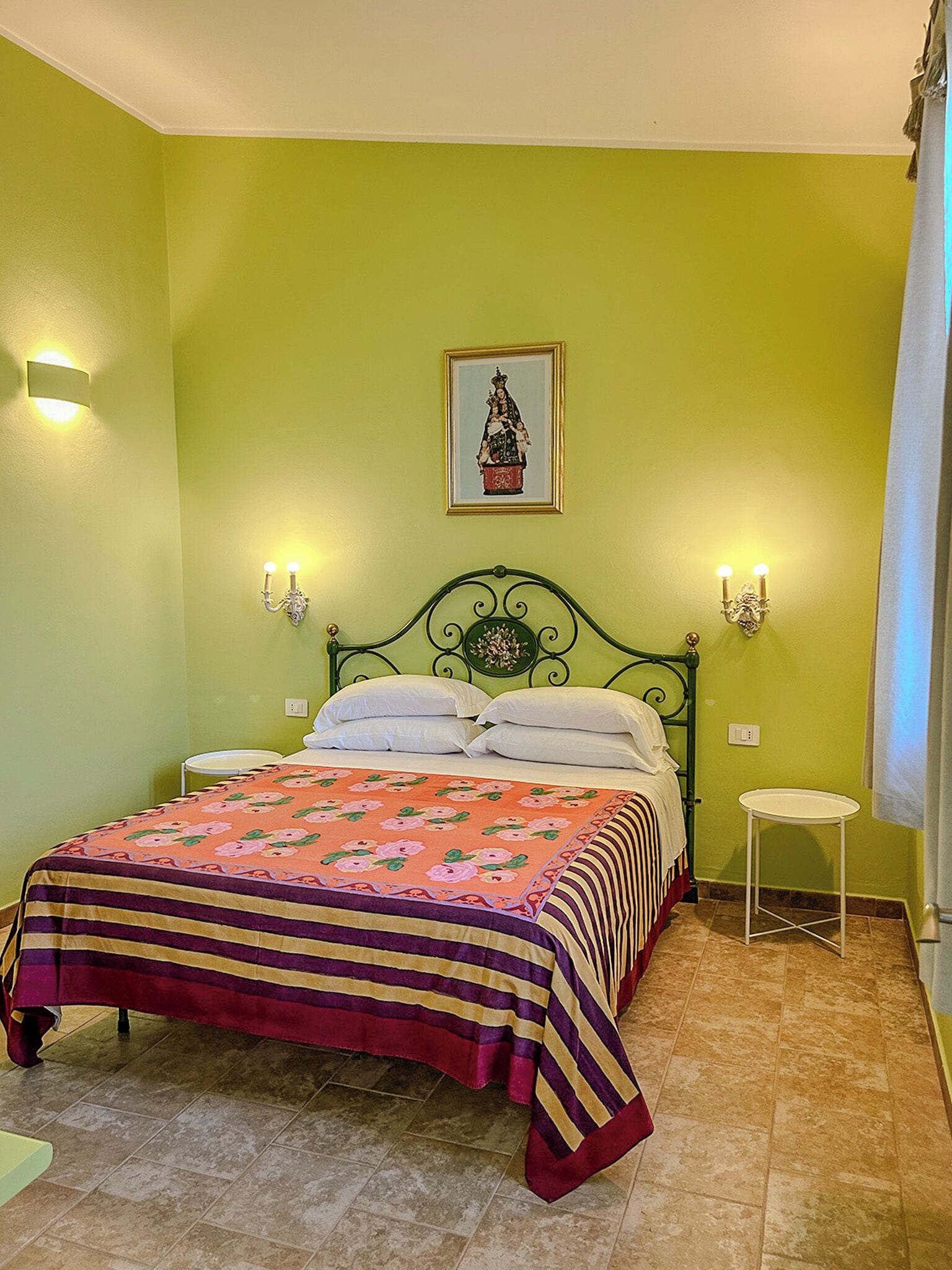 Ein Schlafzimmer mit grüner Wand, einem Bett mit floralem Überwurf, zwei Nachttischen und einem an der Wand hängenden Bild.