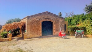 A rustic building with a large arched entrance, a thatched roof structure to the left, and a red scooter parked in front.