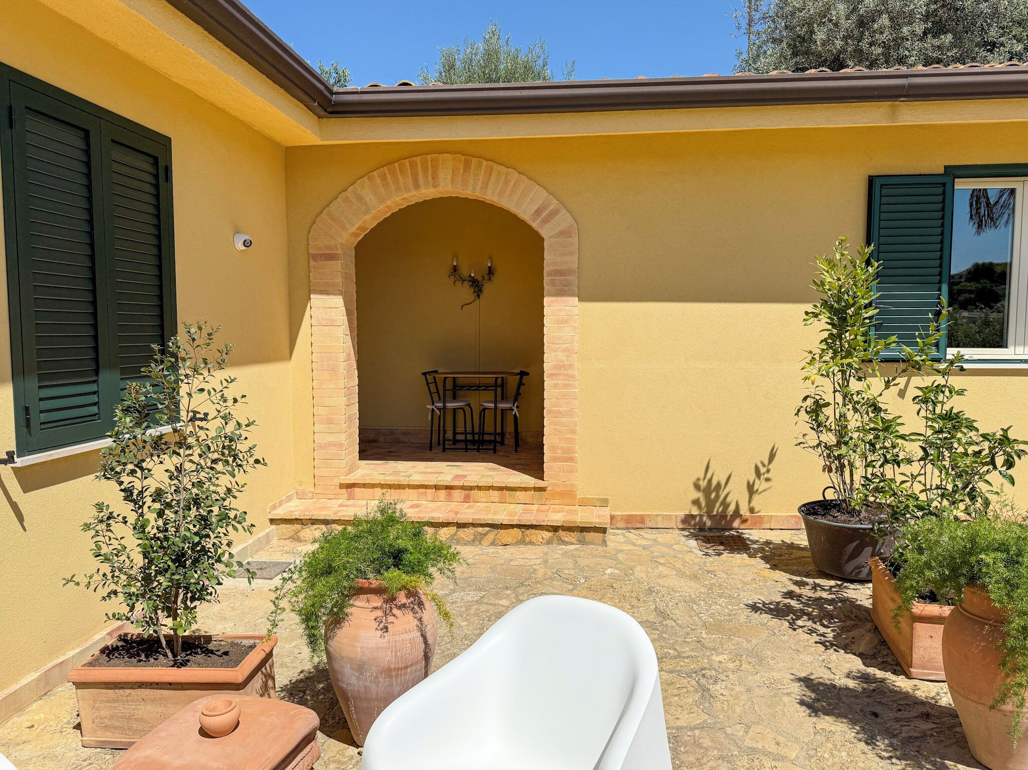 A yellow building with an arched entrance, outdoor seating, and potted plants.