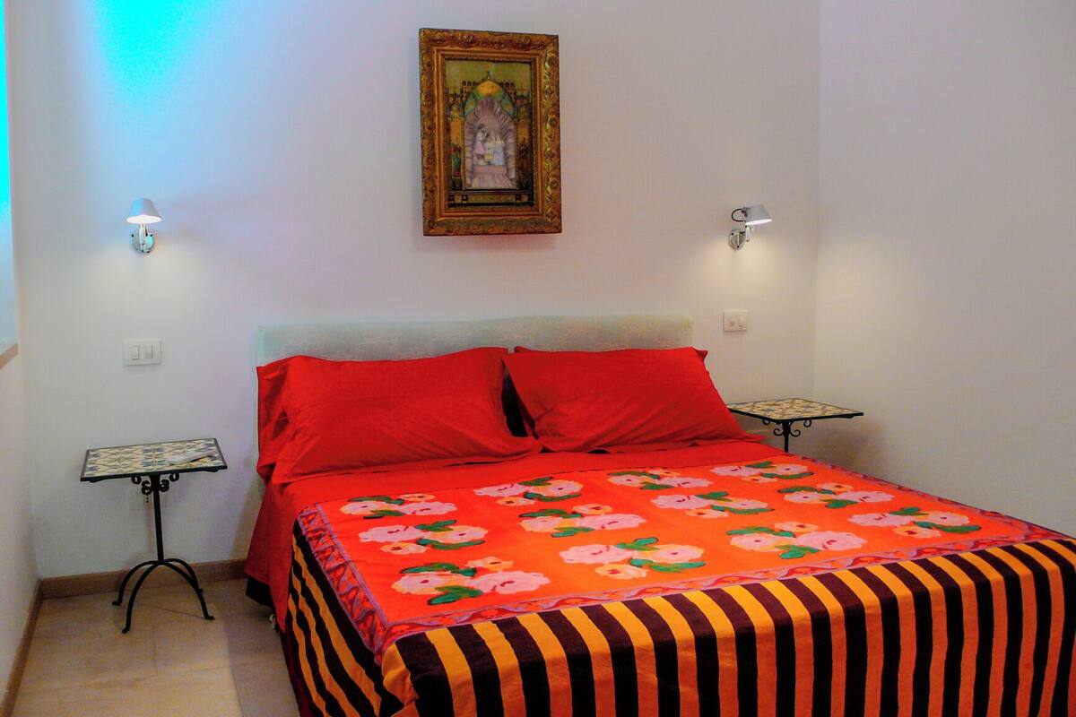 A bedroom with a bed, red pillows, a floral bedspread, two nightstands, and a framed picture on the wall.