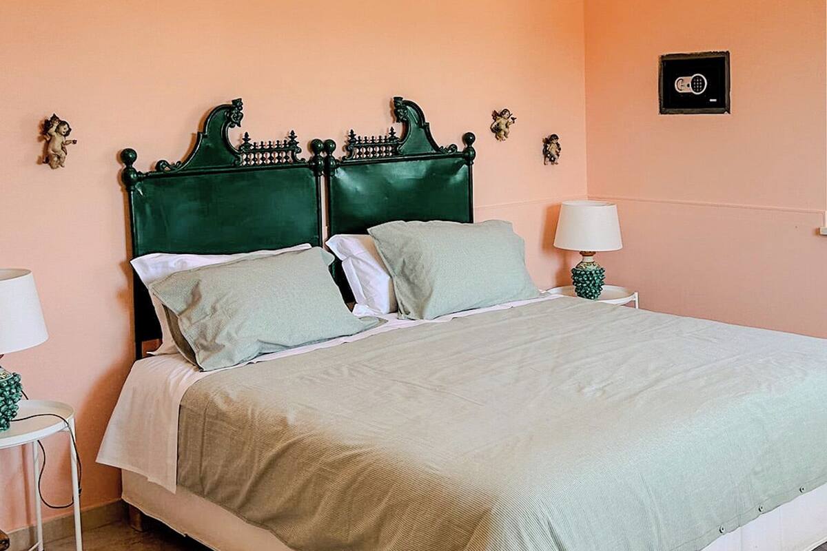 A neatly made bed with a green headboard, two bedside tables with lamps, and a wall clock.