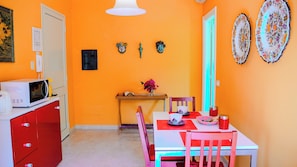 A compact kitchen with a microwave, a red cabinet, and a dining table with chairs. There are decorative plates on the wall and a small shelf with a vase of flowers. - Tenuta Bartoli (Mazzarino)