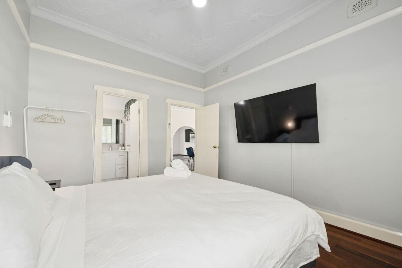 A bedroom with a large bed, a TV mounted on the wall, and a bathroom visible through an open door.