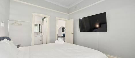 A bedroom with a large bed, a TV mounted on the wall, and a bathroom visible through an open door.