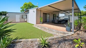 Ein modernes Haus mit überdachter Terrasse, Rasen und Garten mit verschiedenen Pflanzen.