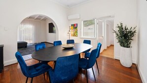 Ein modernes Esszimmer mit einem runden Tisch, blauen Stühlen, einer Kühlpflanze und einem farbenfrohen Gemälde an der Wand.