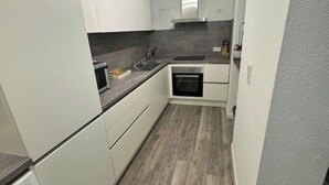 Een kleine keuken met witte kastjes, een magnetron, een spoelbak en een inbouwoven.
