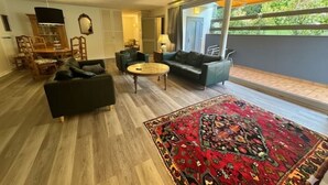 Een moderne woonkamer met een groot raam, een ronde salontafel en een kamerkleed met een patroon.