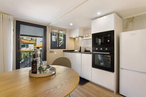 Eine kompakte Küche mit Esstisch, einem schwarzen Backofen, einem weißen Kühlschrank und einem Fenster mit Blick auf Gebäude.
