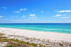 A beach with a clear sky, sandy shore, and a few people walking. - Serenity Shores PCB @ Edgewater - 5th floor, balcony, stunningly updated (Panama City Beach)