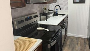 A kitchen with wooden cabinets, a stainless steel refrigerator, a black stove, and a white countertop.