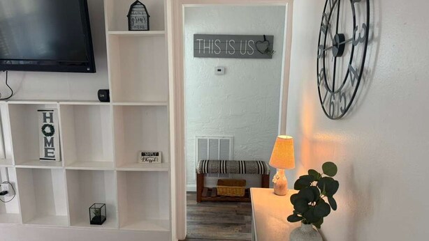 A living room with a TV, shelves, a sign reading "THIS IS US", a lamp, and a plant.