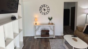 A living room with a white console table, a clock, a television, and a brown leather sofa.