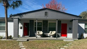 A modern house with a covered porch, two chairs, and a red door.